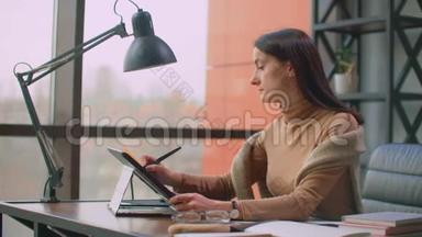 一位女平面设计师在一间有大窗户的办公室工作，用<strong>手写笔</strong>和电脑触摸屏作画